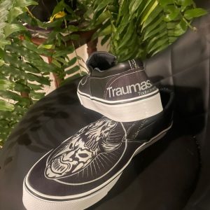 Tenis Slip-On Traumas.mx – Edición "Iconic Black" Lleva el estilo de los encordados a la calle con los Tenis Slip-On de Traumas.mx. Este modelo ofrece una silueta moderna y estilizada, perfecta para quienes prefieren un look más sobrio pero con toda la esencia del pancracio mexicano. Su construcción híbrida combina tela transpirable en el empeine con refuerzos sintéticos, garantizando un calzado resistente y ligero.